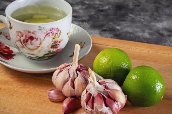 Close-up of herbal tea with garlic and limes on a wooden cutting board, perfect for food photography.